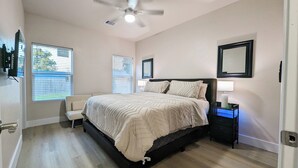 A bedroom with a bed, a ceiling fan, a nightstand with a lamp, and a window with blinds.