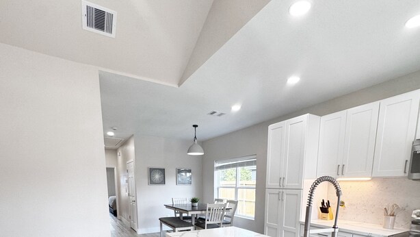 A modern kitchen with a central island, bar stools, and white cabinetry.