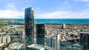 A high-rise building with a glass facade, surrounded by a densely populated urban area with various other buildings. - Stylish City Apartment with Expanding City Views (Southbank)