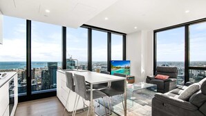 A modern living room with a dining area, large windows, a flat-screen TV, and a city view. - Stylish City Apartment with Expanding City Views (Southbank)
