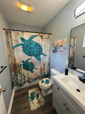 Une salle de bain avec un rideau de douche à motifs de tortues de mer, des toilettes, un lavabo et un petit tapis.