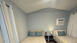 A bedroom with two single beds, a sofa, a ceiling light, and an air conditioning unit.