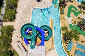 An aerial view of a swimming pool area with a water slide, surrounded by palm trees and a pebble beach. - Elegant 2BR in Storey Lake, Top Location (Kissimmee)