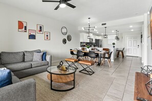 A modern living room with a sofa, coffee table, and dining area with chairs and a kitchen in the background.