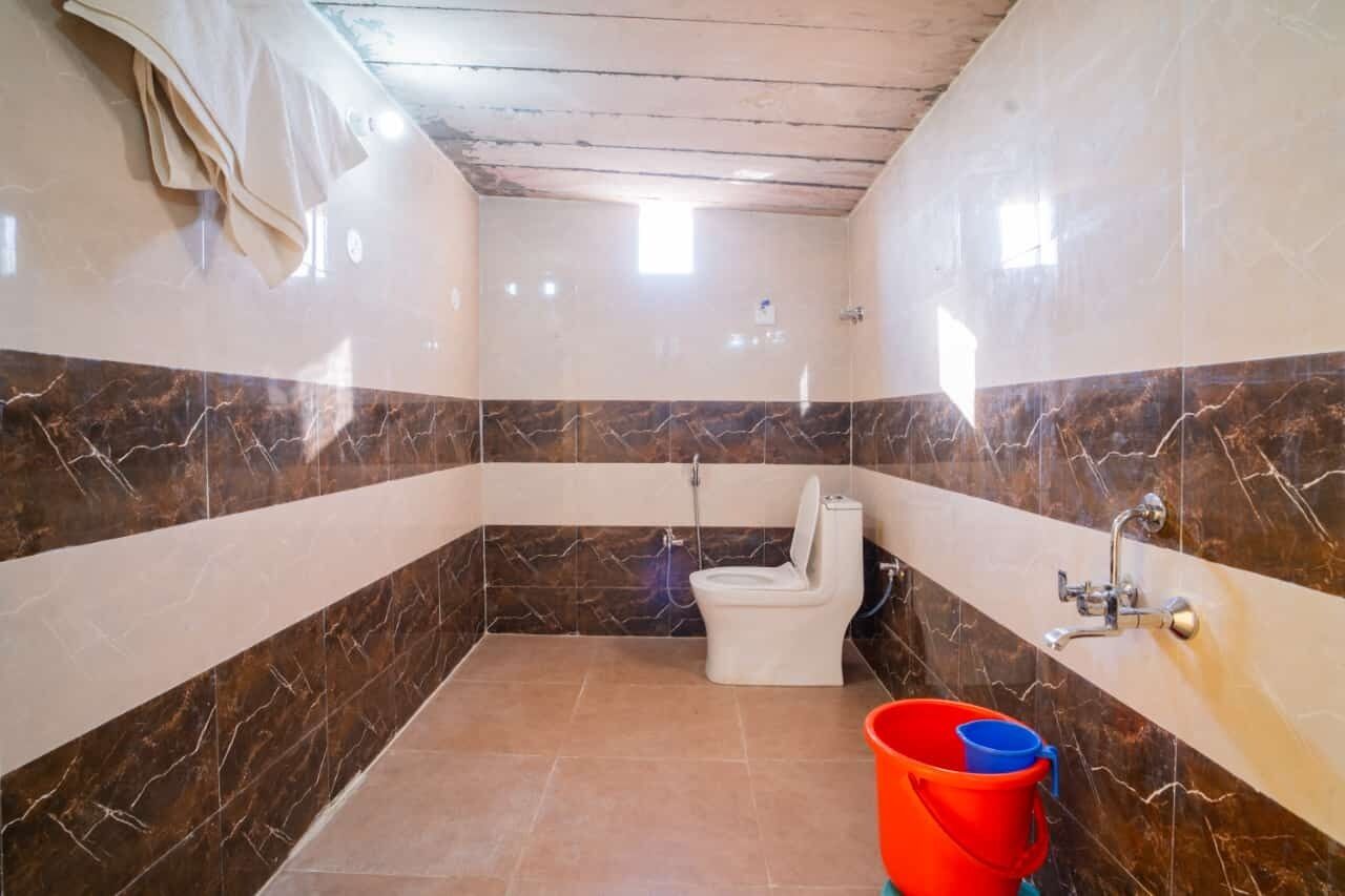 A bathroom with a toilet, shower, and a red bucket.