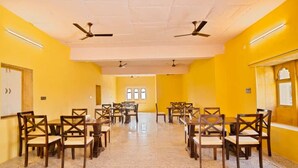 A conference room with yellow walls, multiple tables and chairs, ceiling fans, and a whiteboard. - Saira Heritage Resort (Jaisalmer)