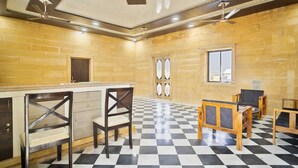A spacious room with a checkered floor, a wooden bar, and a seating area with chairs and a table. - Saira Heritage Resort (Jaisalmer)