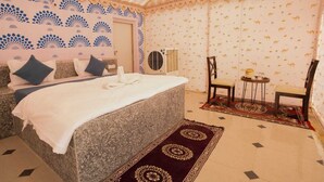A bedroom with a bed, two chairs, a small table, and a decorative rug. - Saira Heritage Resort (Jaisalmer)