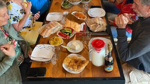 A long communal dining table with various dishes and drinks, surrounded by seated guests.