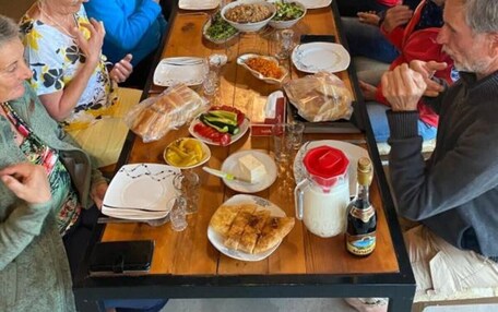 A long communal dining table with various dishes and drinks, surrounded by seated guests.