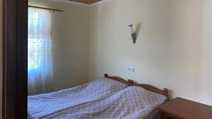 A bedroom with a wooden ceiling, a bed with patterned bedding, a bedside table, and a wall-mounted light fixture.