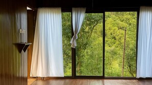 Quarto com uma janela grande, piso de madeira e cama com lençóis brancos.