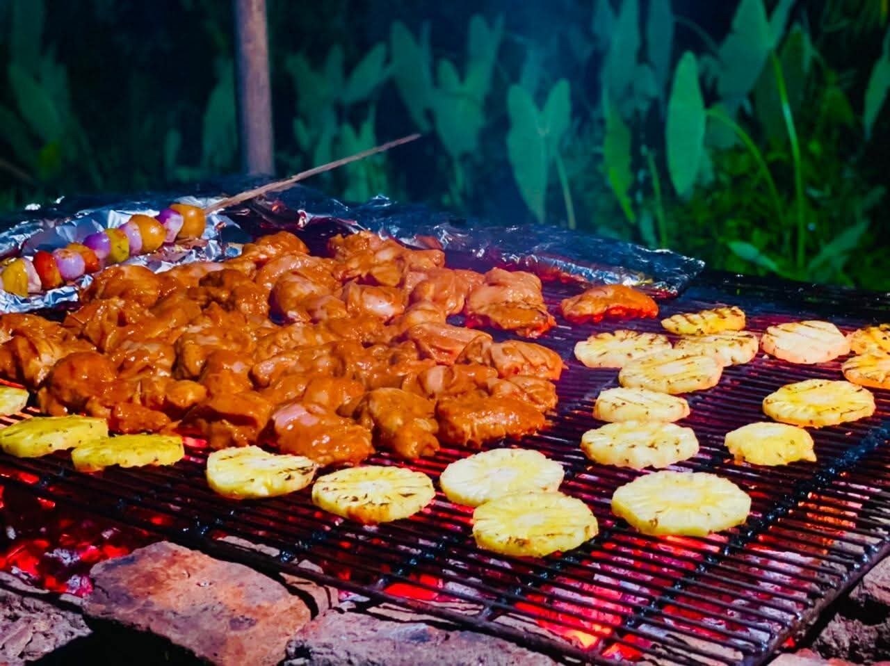 Una parrilla con diversos tipos de carne y trozos de piña asándose.