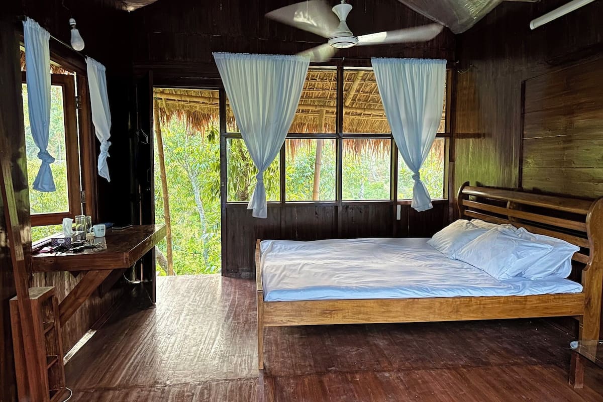 Una habitación de madera con una cama, un escritorio y una ventana con cortinas.