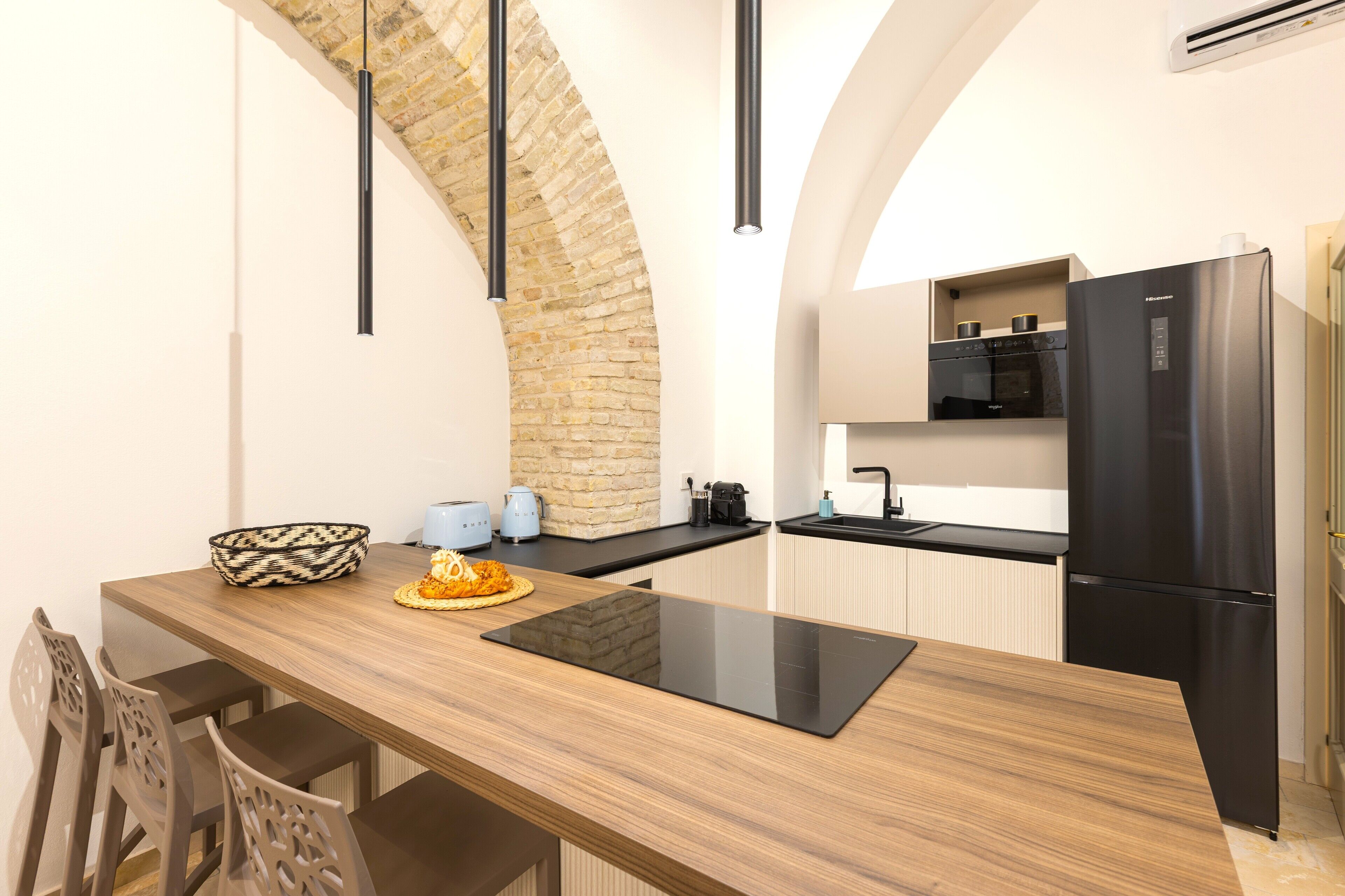 A modern kitchen with a wooden island, black appliances, and a stone wall.