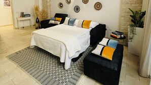 Un dormitori amb un llit gran, un sofà negre, un faldilla estampada i una paret de pedra amb decorations circulars.