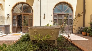 Un pati amb una gran jardiniera de pedra, finestres arquejades i plantes en testos.