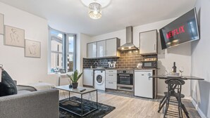 A modern apartment with a kitchen, living area, and a TV displaying 'NETFLIX'. - Central Location • Edgbaston Village / Broadway Plaza | Fast Wi-Fi | Sleeps 4 (Birmingham)