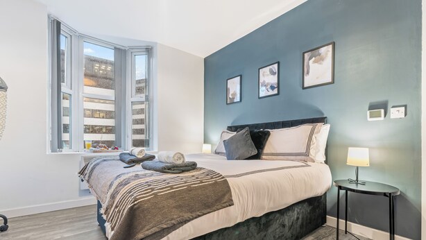 A modern bedroom with a large bed, a window with a view of a building, and a bedside table with a lamp. - Central Location • Edgbaston Village / Broadway Plaza | Fast Wi-Fi | Sleeps 4 (Birmingham)