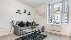 A modern living room with a grey sofa, black cushions, a coffee table, a black furry rug, and a window with a view of buildings. - Central Location • Edgbaston Village / Broadway Plaza | Fast Wi-Fi | Sleeps 4 (Birmingham)