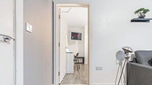 A modern living room with a grey sofa, a small table, and a floor lamp. A TV is mounted on the wall in the background. - Central Location • Edgbaston Village / Broadway Plaza | Fast Wi-Fi | Sleeps 4 (Birmingham)