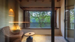 Un balcon avec un fauteuil en osier et une petite table, une vue sur les arbres et une porte vitrée.