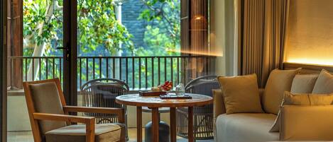 Habitación de hotel con balcón, una mesa redonda de madera, un sofá y una silla.