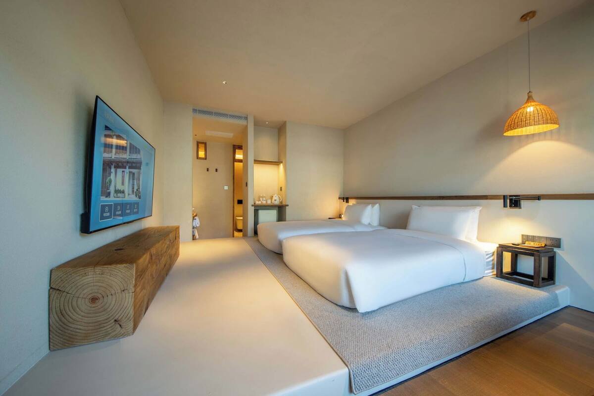 A modern hotel room with a large bed, a wooden headboard, a bedside table, and a hanging light fixture.