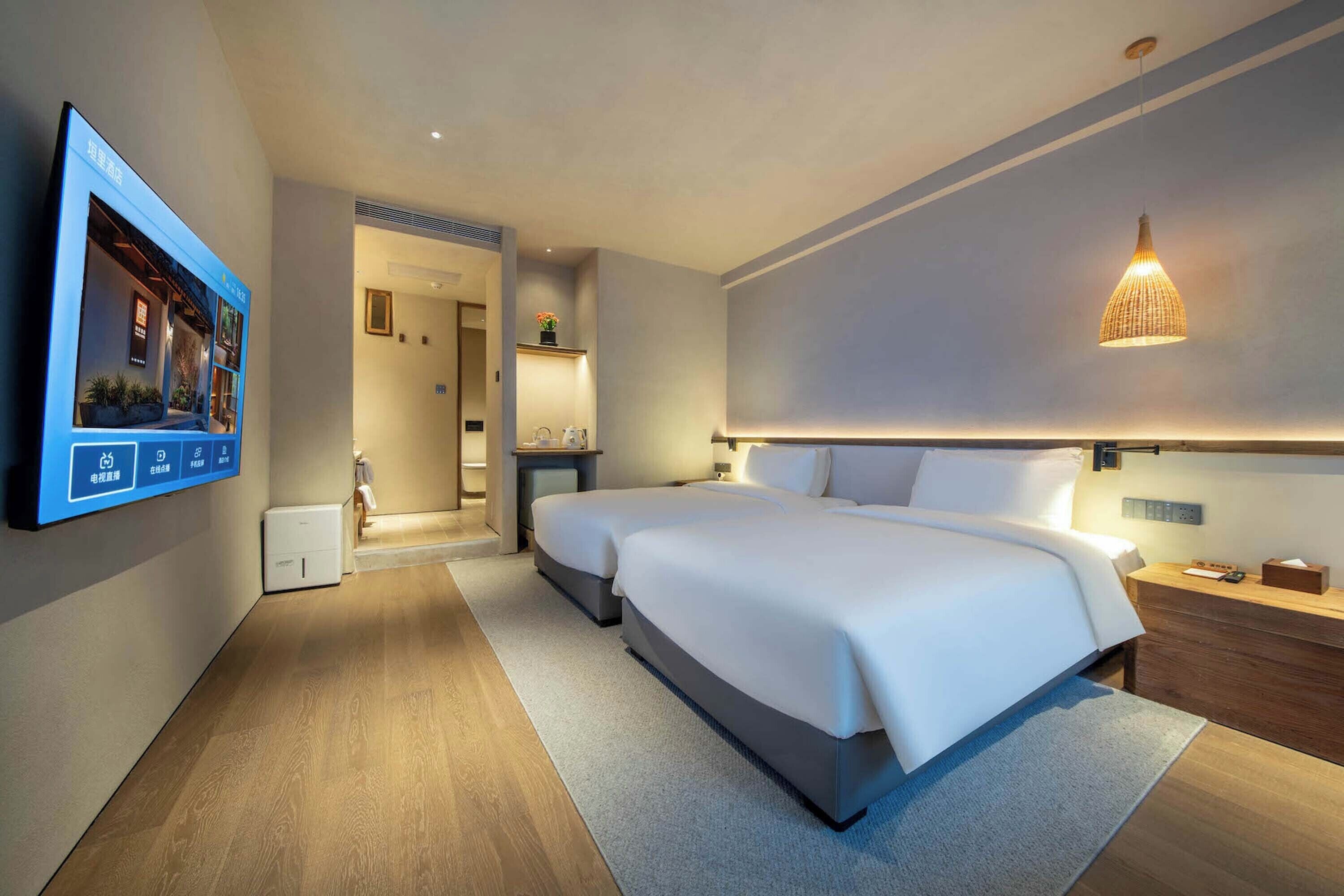 Una habitación de hotel moderna con una cama grande, mesitas de noche, un televisor de pantalla plana y una lámpara de pared.