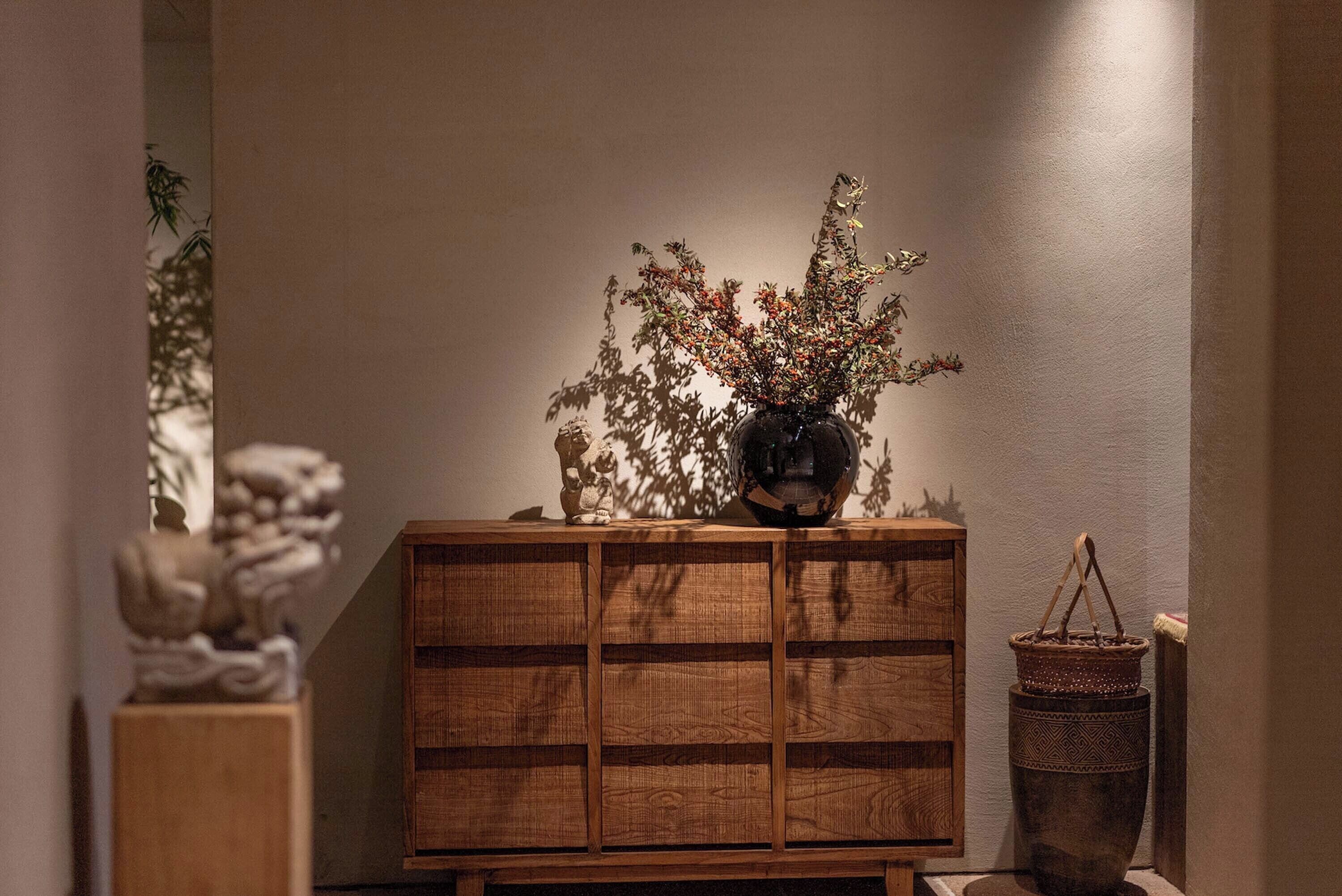 A wooden cabinet with a vase of dried branches and a small statue on top.