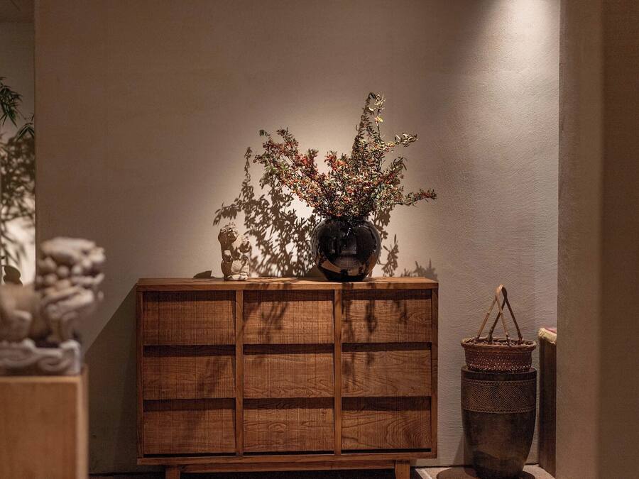 A wooden cabinet with a vase of dried branches and a small statue on top.