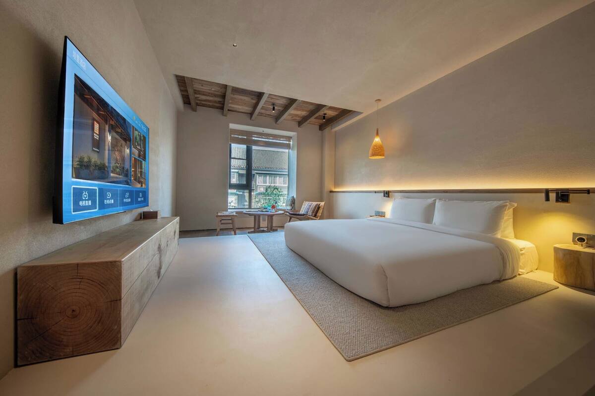 A modern bedroom with a large bed, a TV mounted on the wall, and a wooden bench.