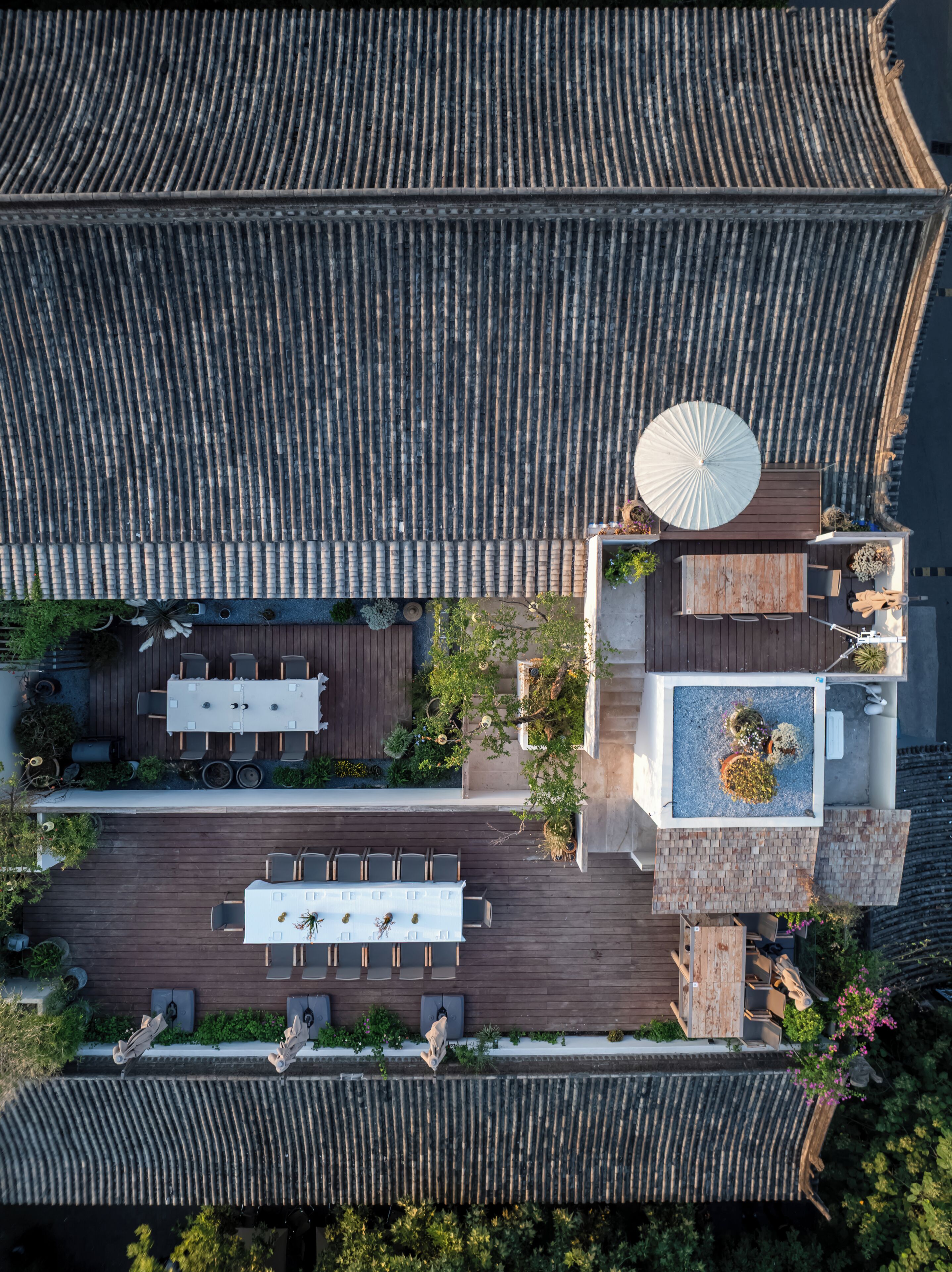 An aerial view of a rooftop terrace with a dining area, a small garden, and a seating area with a large umbrella.