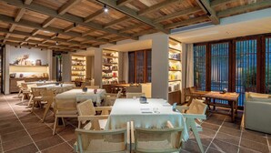 Une salle à manger spacieuse, avec des tables et des chaises en bois, un plafond haut avec des poutres apparentes et de grandes fenêtres offrant une vue sur l’extérieur.