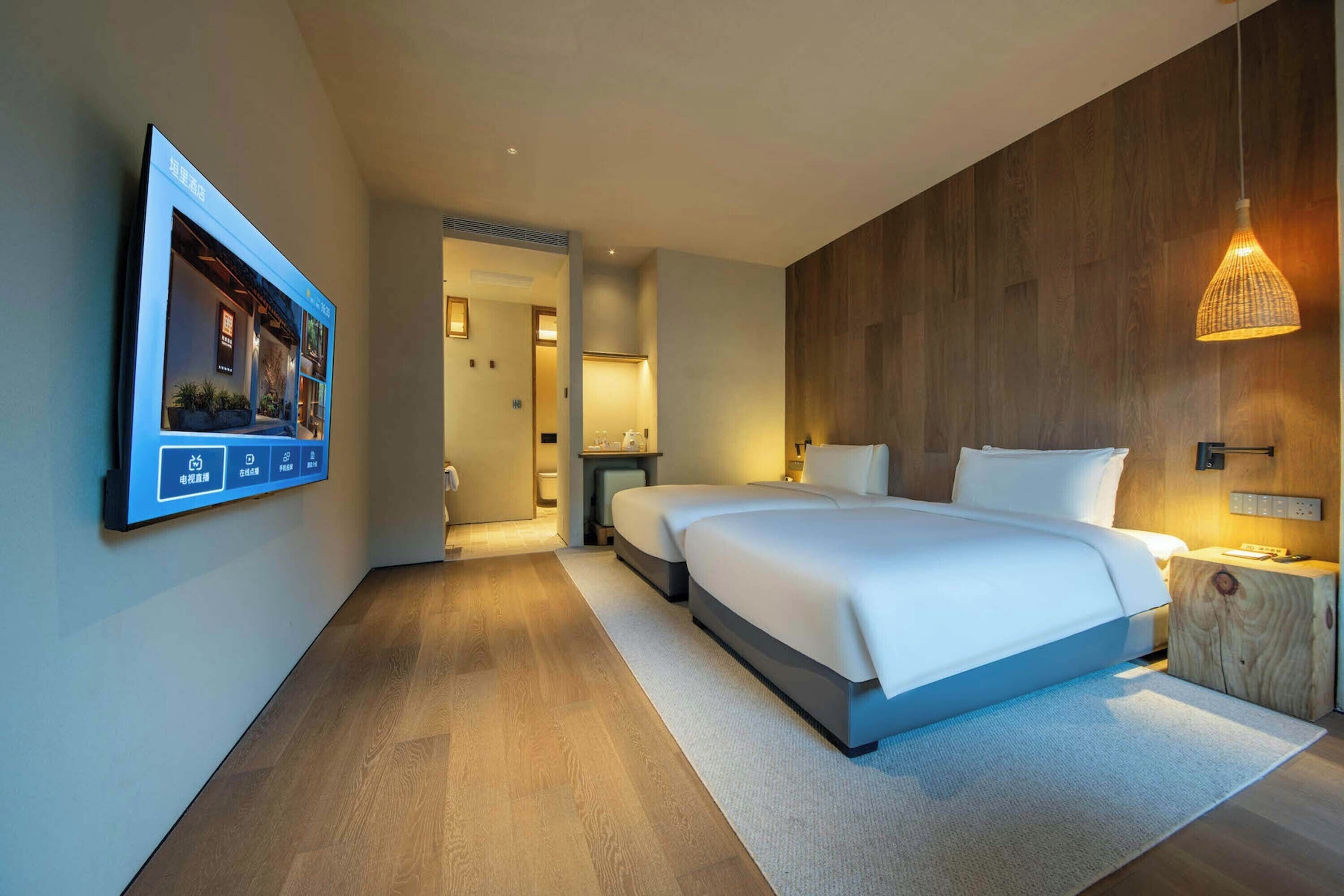 Una habitación de hotel moderna con una cama grande, mesitas de noche, un televisor montado en la pared y una pared de acento de madera.