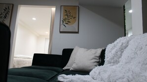 Una sala de estar moderna con un sofá verde oscuro, un edredón blanco y mullido, y un cuadro enmarcado en la pared.