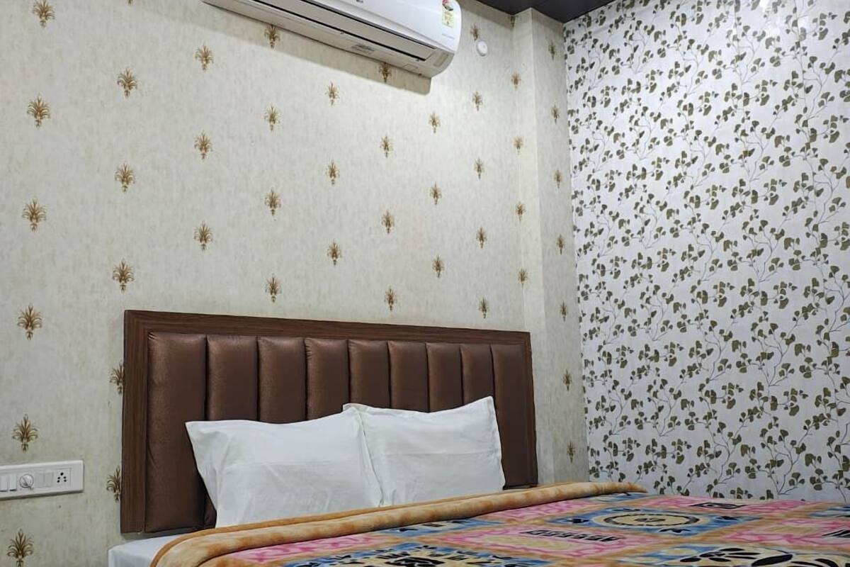 A hotel room with a bed, an air conditioning unit, a ceiling fan, and patterned wallpaper.