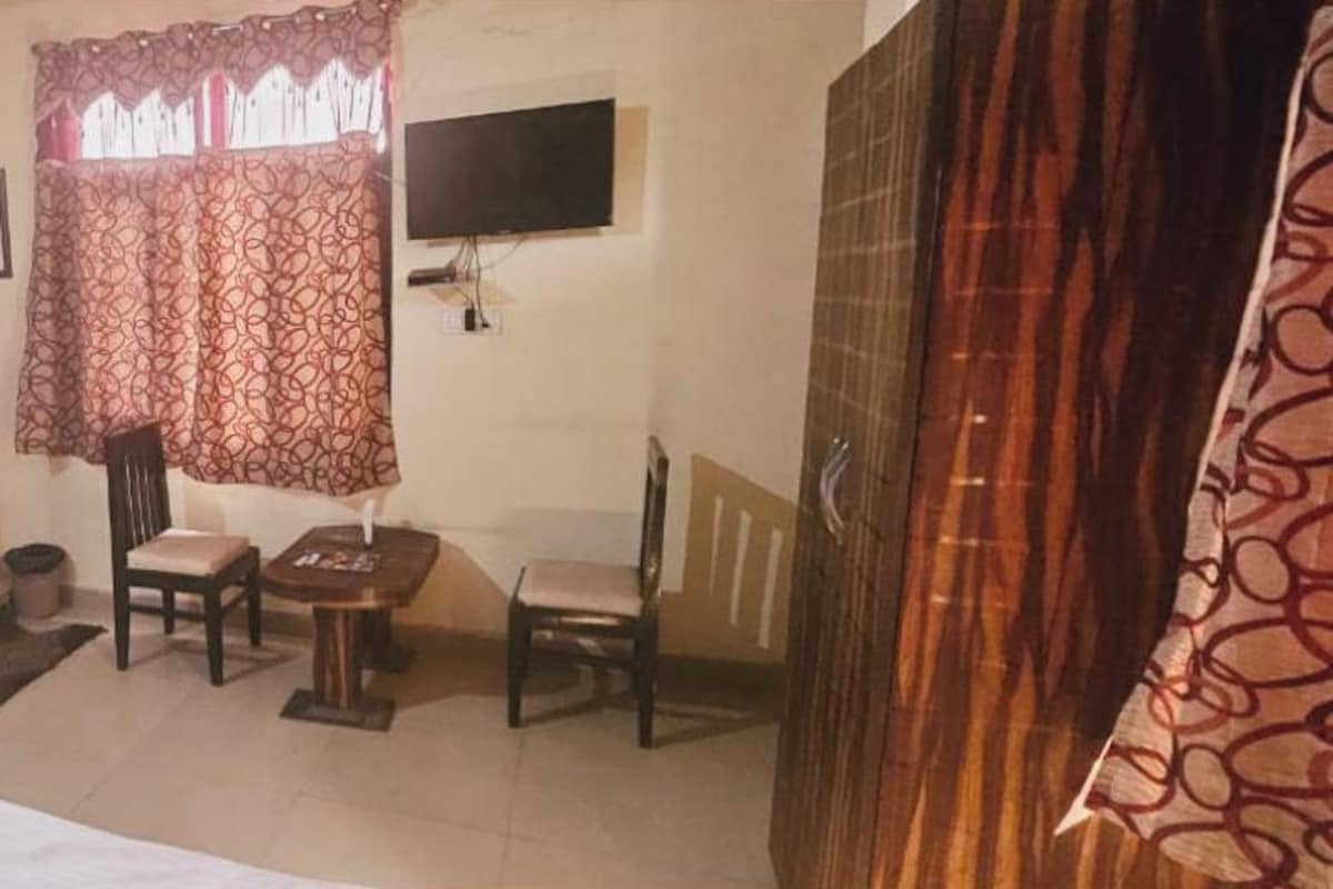 Habitación de hotel con cama, una mesita, dos sillas, televisión y ventana con cortinas estampadas.