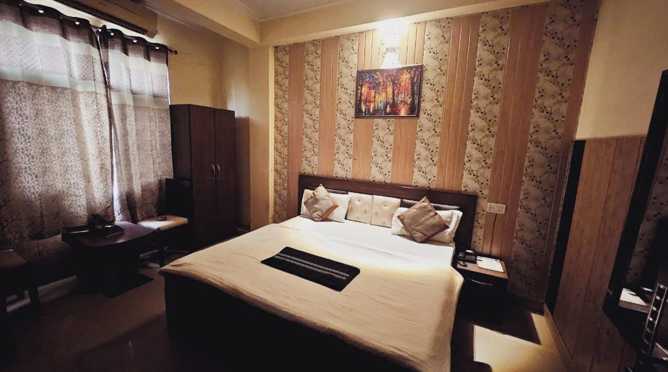 A hotel room with a bed, a desk, a chair, a nightstand, and a TV.