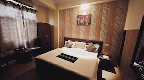 Habitación de hotel con cama, escritorio, silla, mesita de noche y televisión.