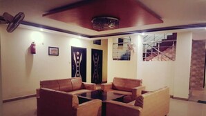 A room with two leather sofas and a central coffee table, a ceiling fan, a fire extinguisher, and a staircase with a view of the outside. - Hotel Golden Village Sidcul Haridwar (Haridwar)