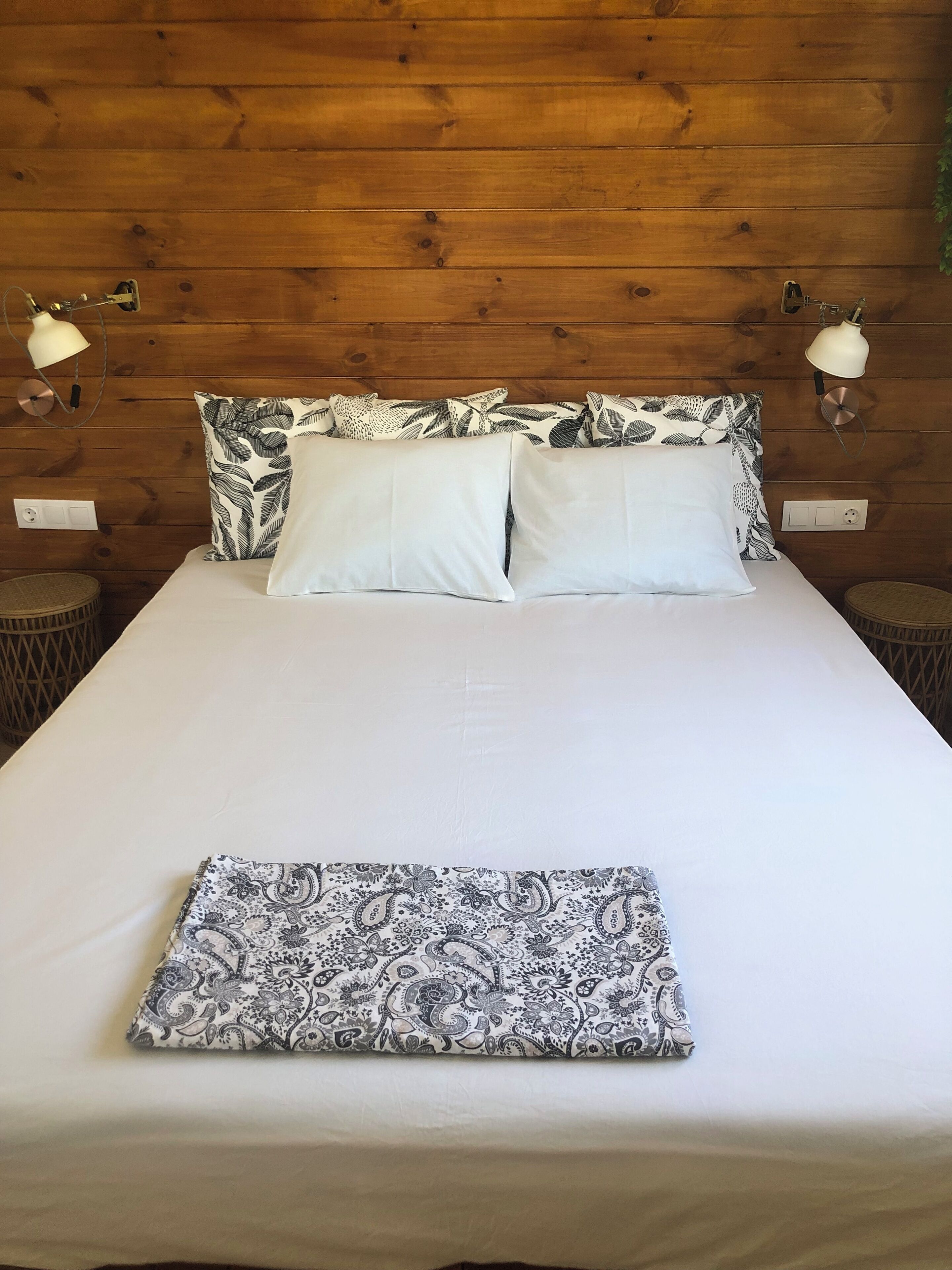 Un lit avec du linge de lit blanc, deux oreillers ornés d’un motif de feuilles et un coussin à motifs cachemire posé sur le lit.