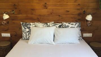 Un lit avec du linge de lit blanc, deux oreillers ornés d’un motif de feuilles et un coussin à motifs cachemire posé sur le lit.