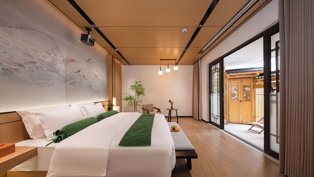 Habitación de hotel moderna con una cama grande, piso de madera, un ventanal y vistas al exterior.
