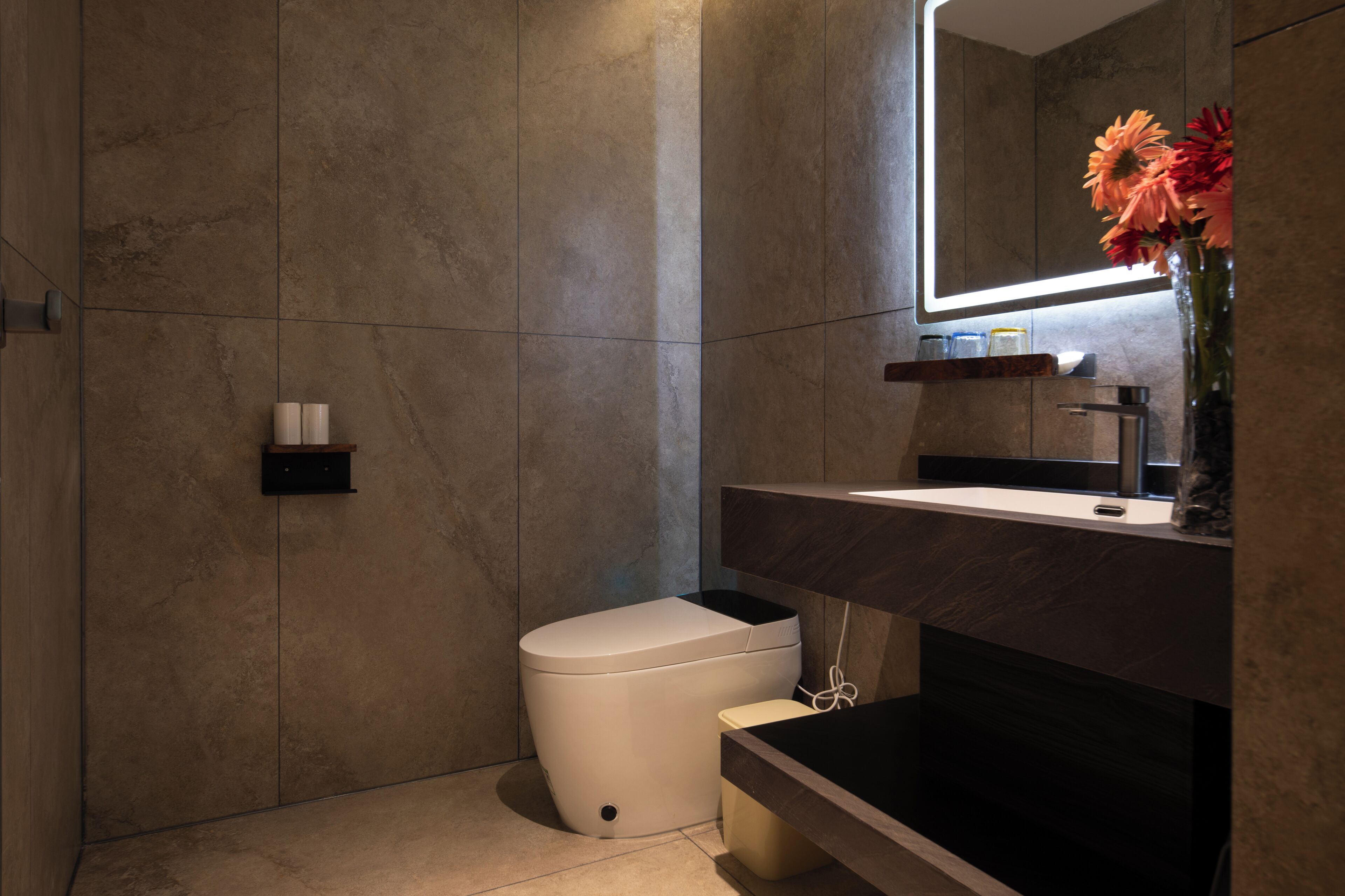 Ein modernes Badezimmer mit einer weißen Toilette, einem dunklen Waschbecken und einem Spiegel darüber.