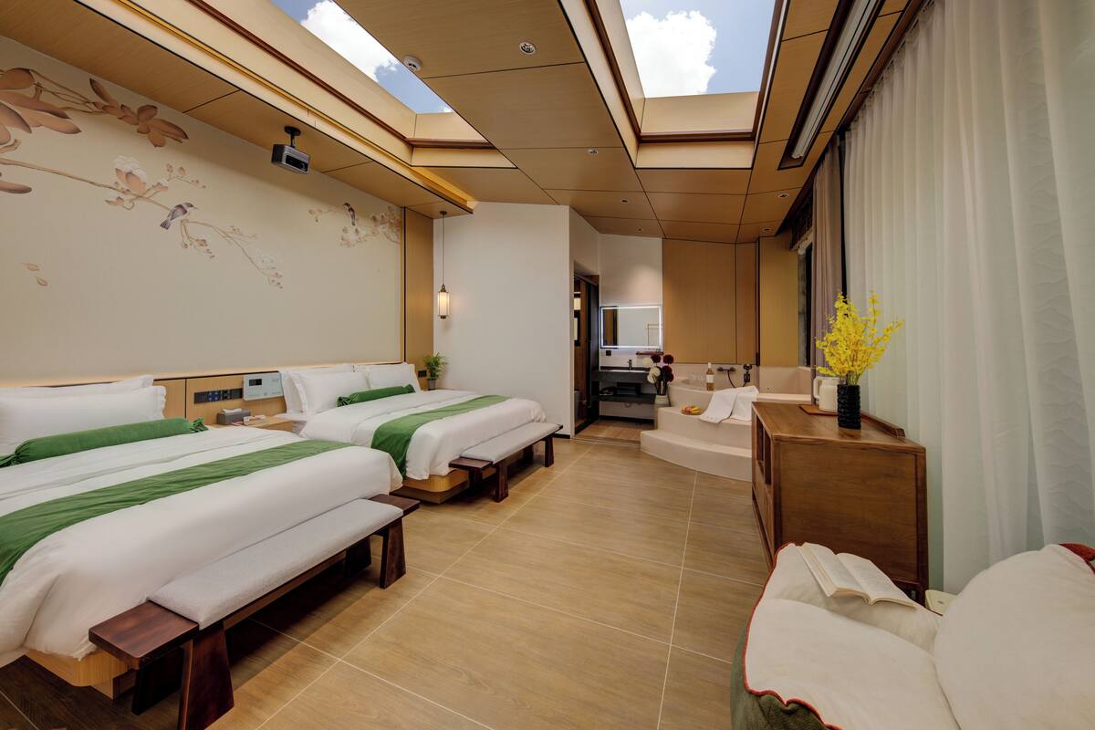 Habitación de hotel con dos camas, zona de estar, baño y vista al cielo.