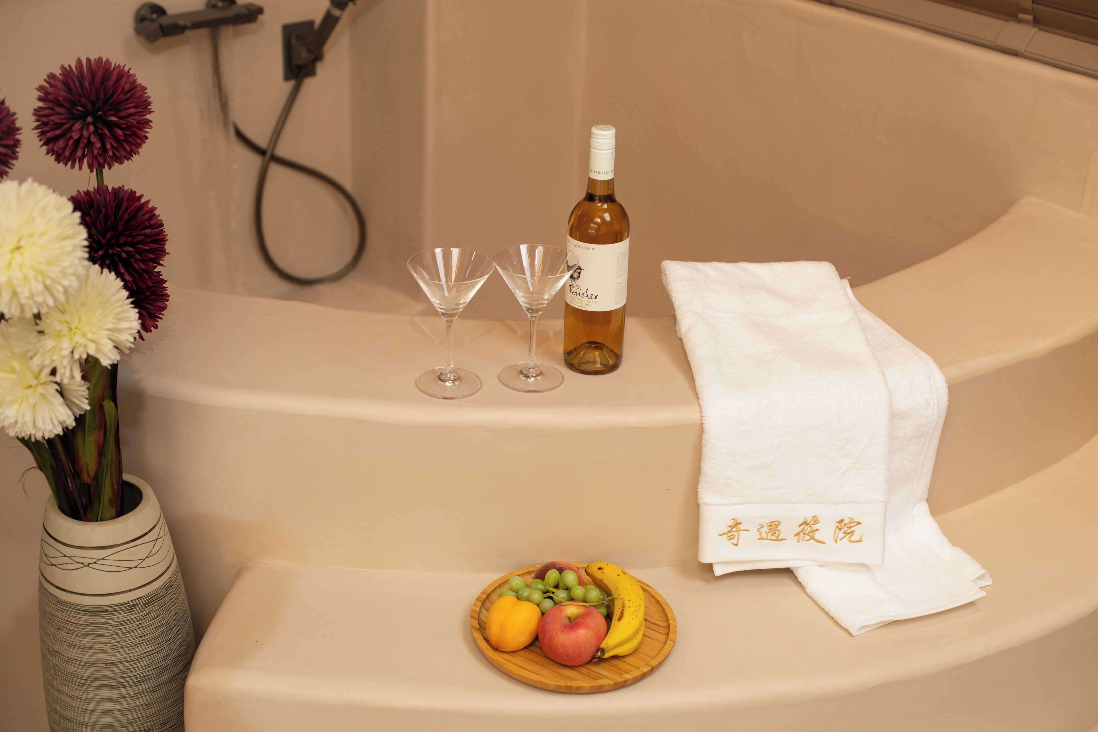 Ein Badezimmer mit einer Badewanne, einer Weinflasche, zwei Gläsern, einer Obstschale und einem Blumenstrauß.
