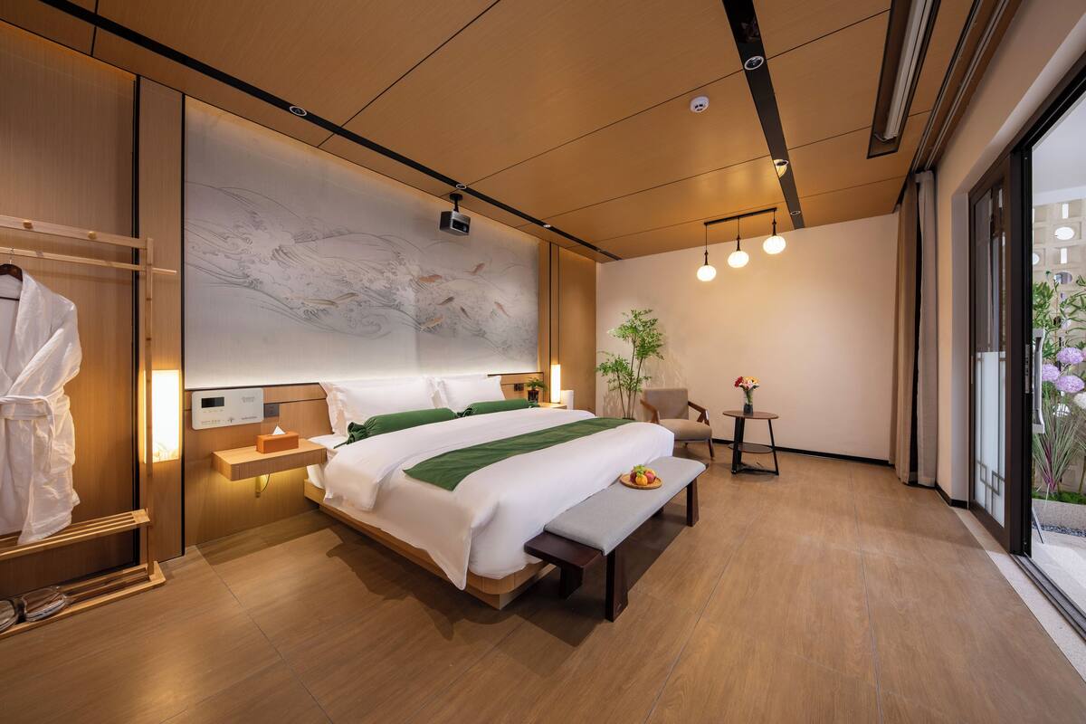 Una habitación de hotel moderna con una cama grande, mesitas de noche, un banco y vistas al exterior.