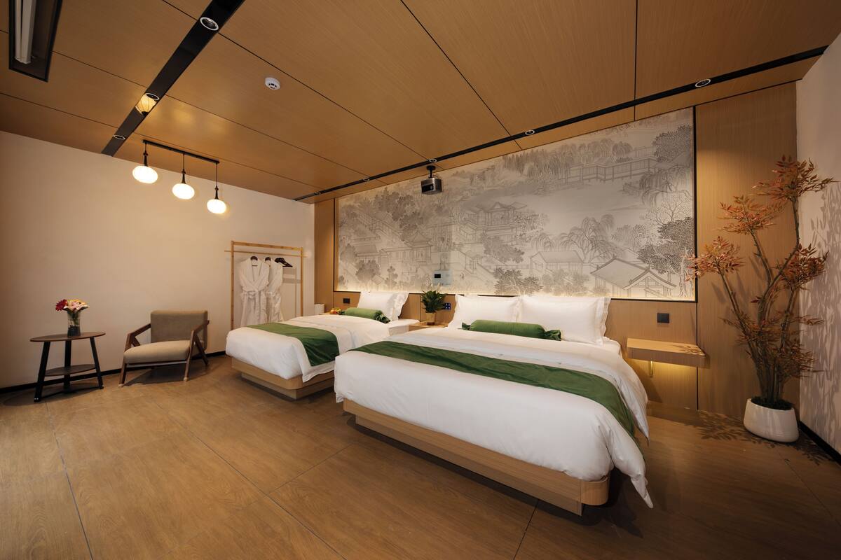 Una habitación de hotel moderna con dos camas, una silla, una mesita y un mural grande en la pared.