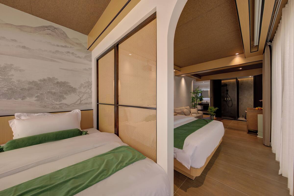 Habitación de hotel con dos camas, un cuadro grande en la pared y una puerta corredera que da a un baño.